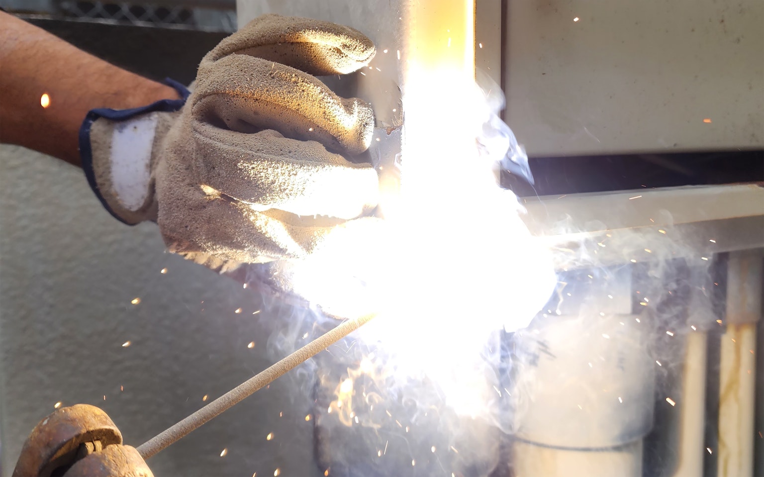 Una mano con guante realizando trabajo de soldadura con chispas brillantes