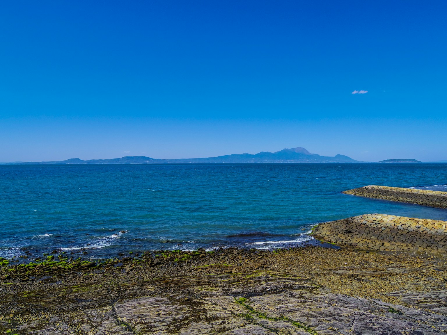Vista escénica del mar azul y cielo despejado costa rocosa con montañas distantes