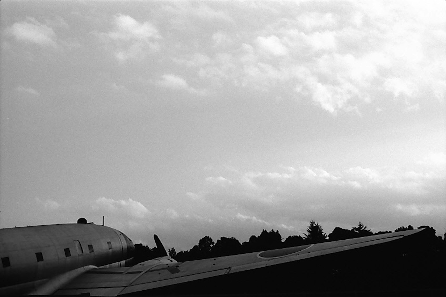 Black and white image showing clouds in the sky and part of an airplane wing