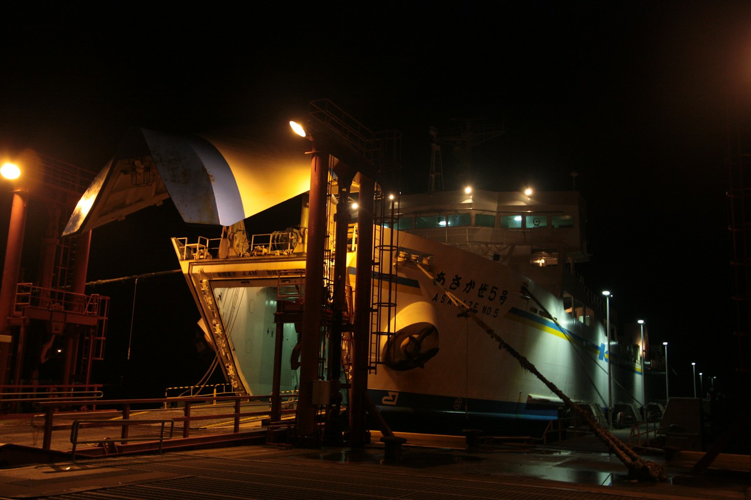Gran barco atracado de noche con lado iluminado y rampa