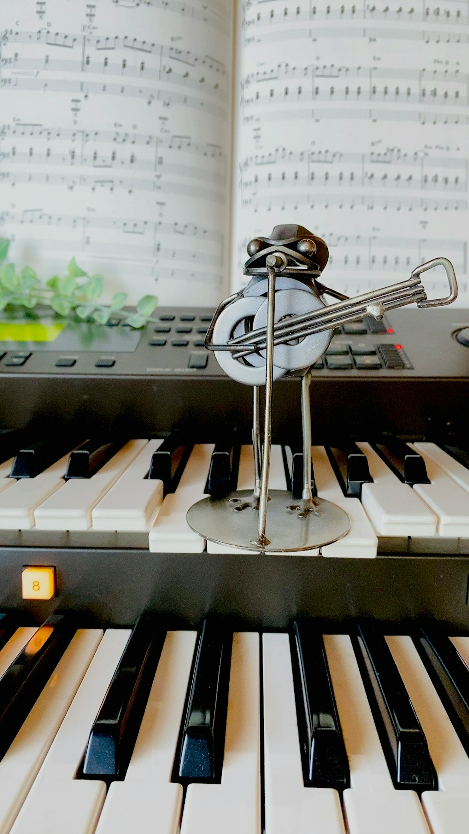 Figura di musicista in metallo unica in piedi sui tasti del pianoforte con spartito sullo sfondo