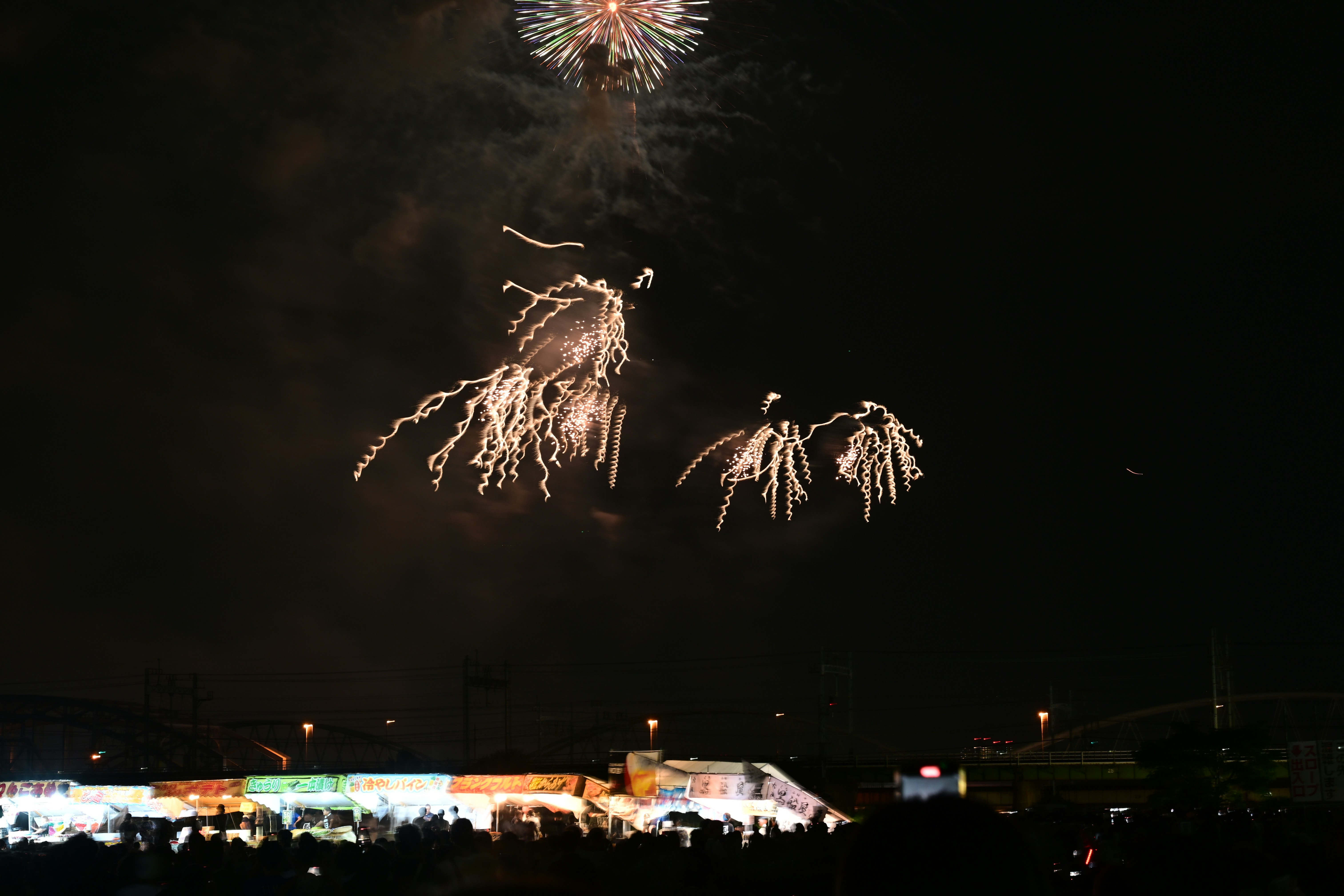 夜空に打ち上がる花火と屋台のある会場の風景