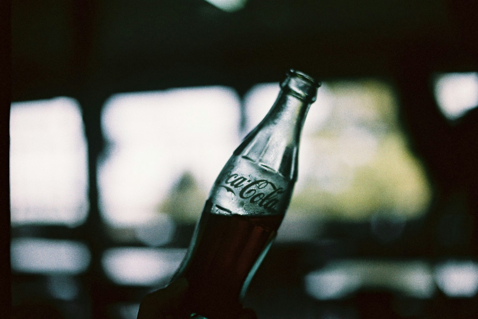 Una mano che tiene una bottiglia di Coca-Cola con uno sfondo sfocato
