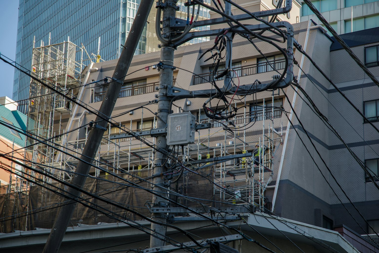 Urban landscape with intersecting power poles and wires alongside a construction site