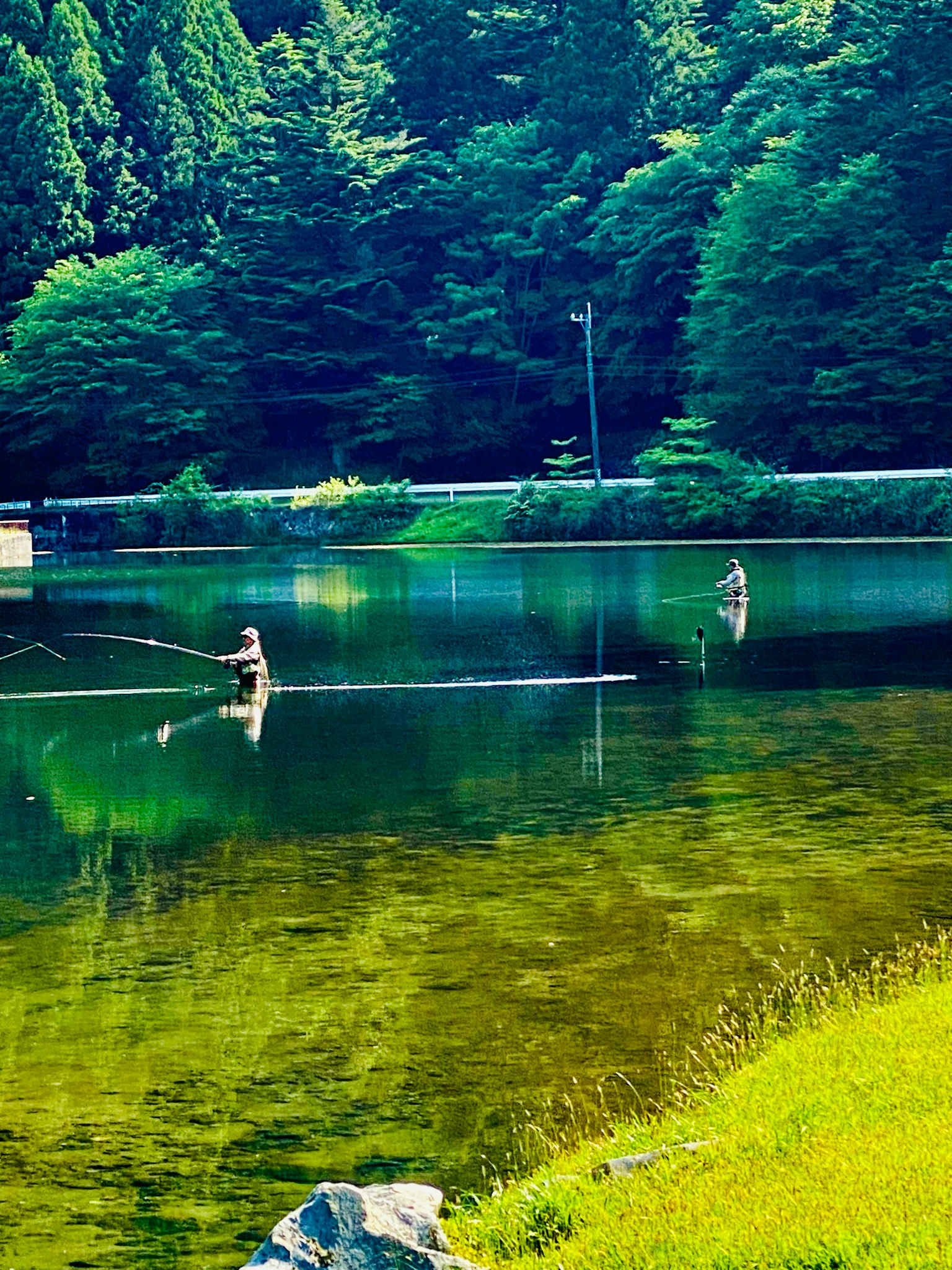 Ein ruhiger See mit einem Fischer, der auf einem Baumstamm steht, umgeben von üppigem Grün