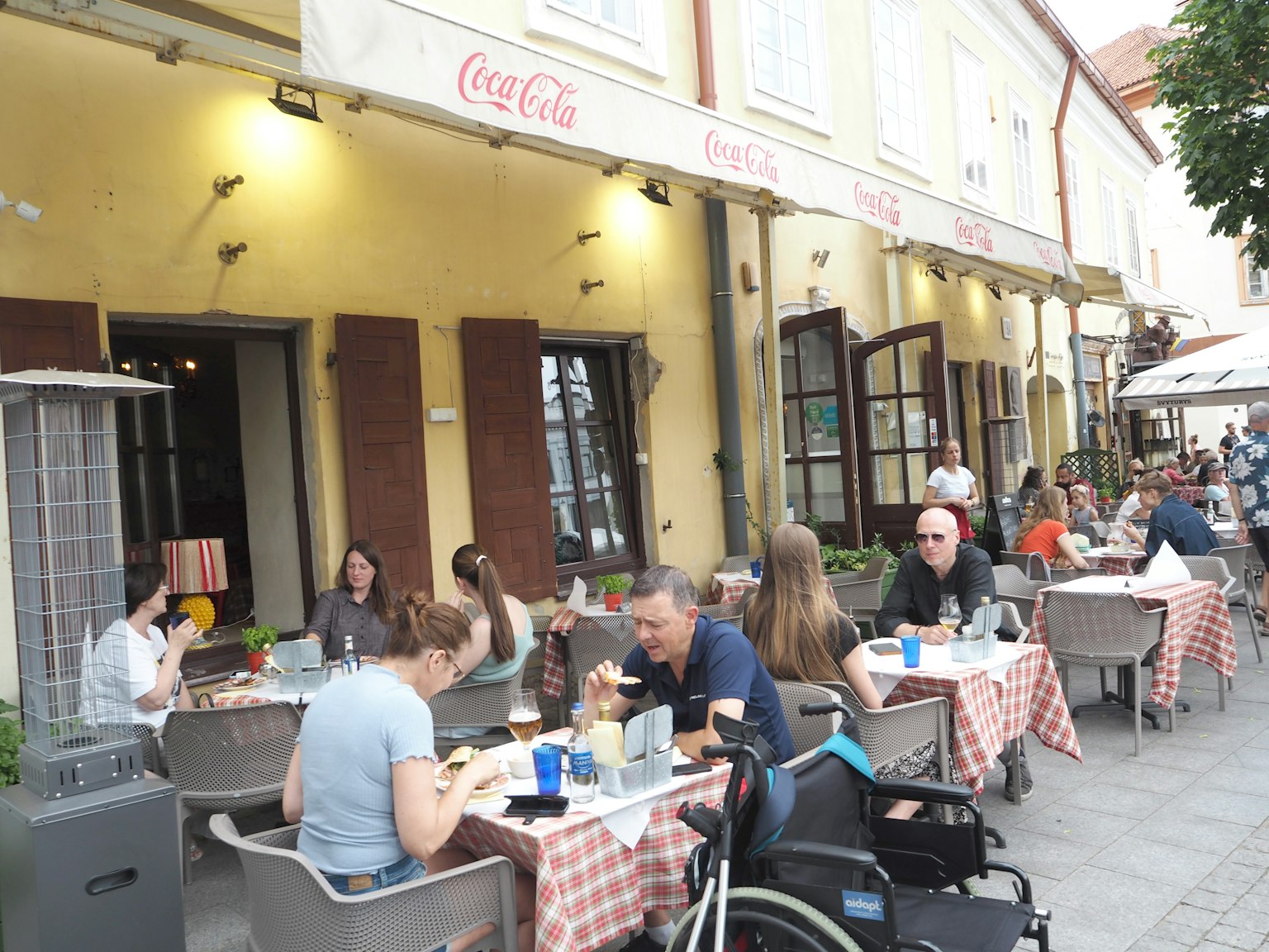 Scena di ristorante all'aperto con clienti che pranzano e un'insegna Coca-Cola