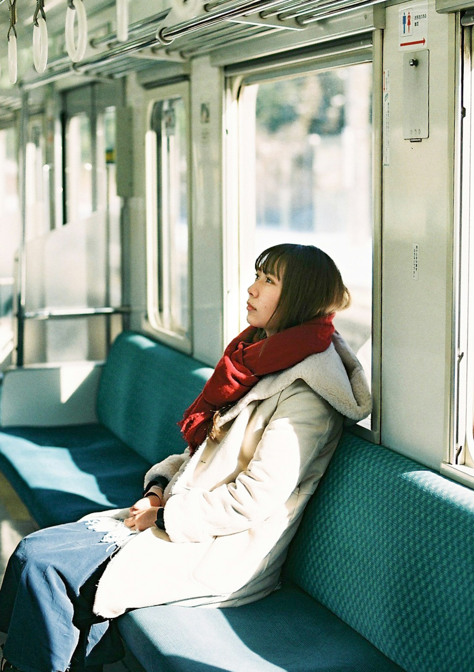 Una mujer sentada tranquilamente en un tren con una bufanda roja junto a la ventana