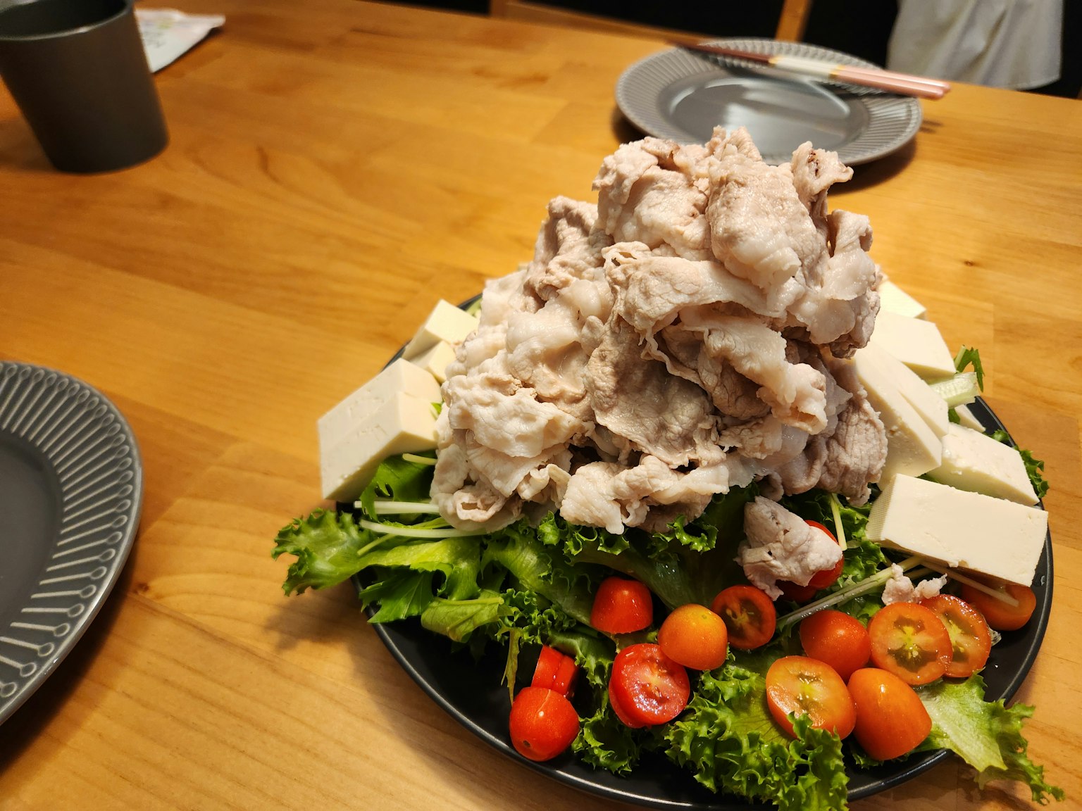 Un plato con cerdo y tofu apilados sobre una cama de ensalada y tomates cherry