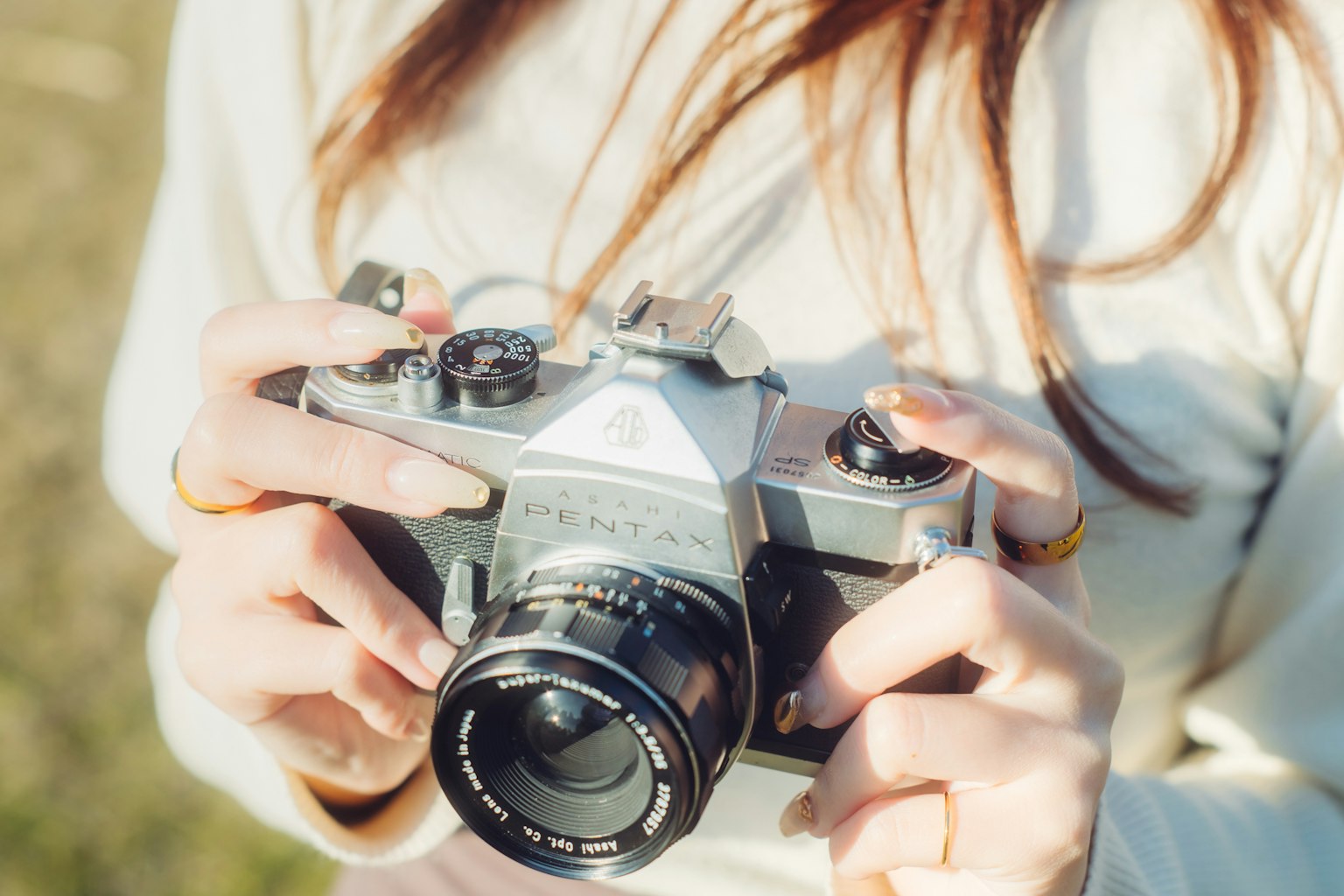 A woman holding a silver camera in a natural outdoor setting