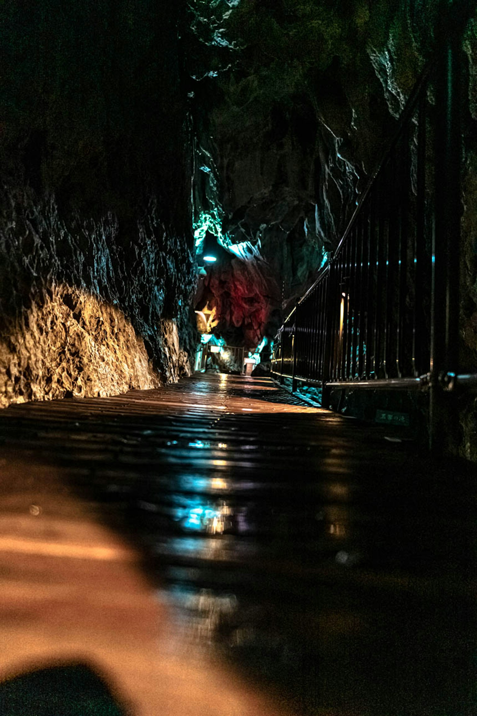 A dimly lit cave pathway with wet ground and reflective surfaces