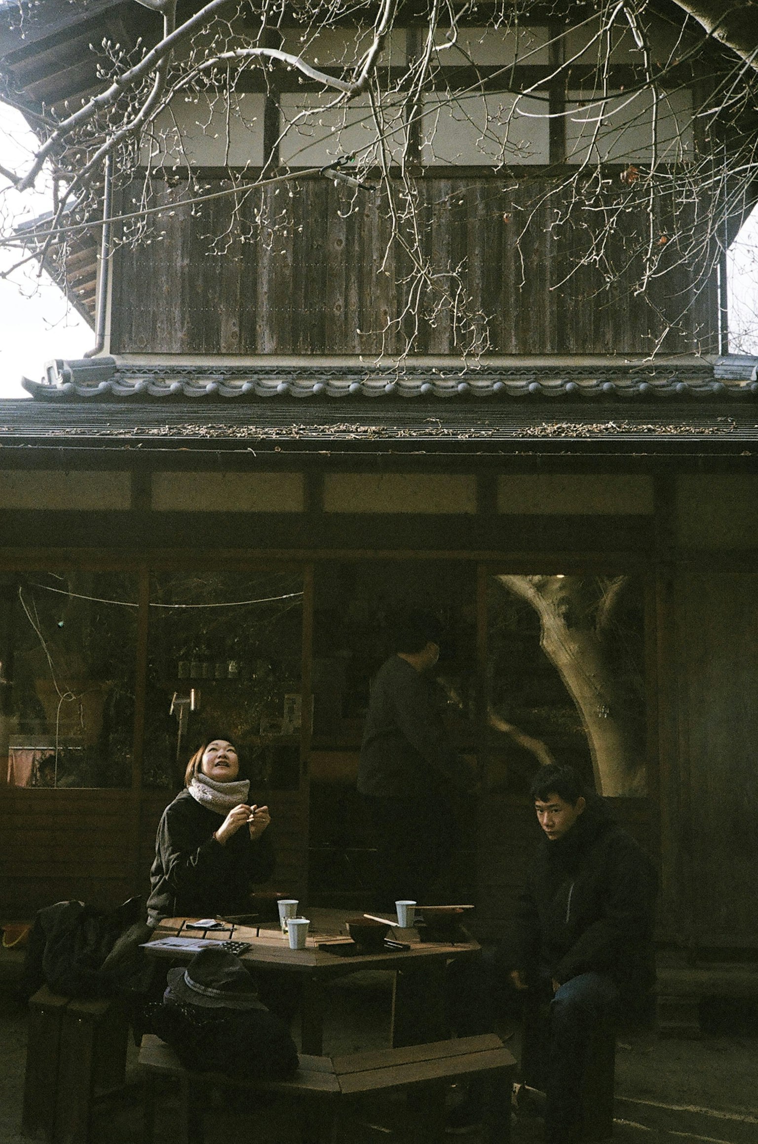 木造の建物の前で二人の人が座っているテーブルに飲み物が置かれている