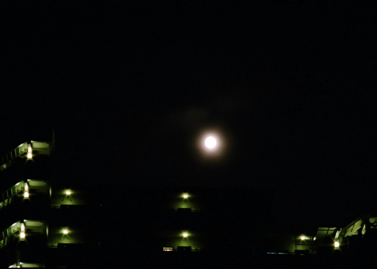 Luna llena brillante en el cielo nocturno con siluetas de edificios oscuros