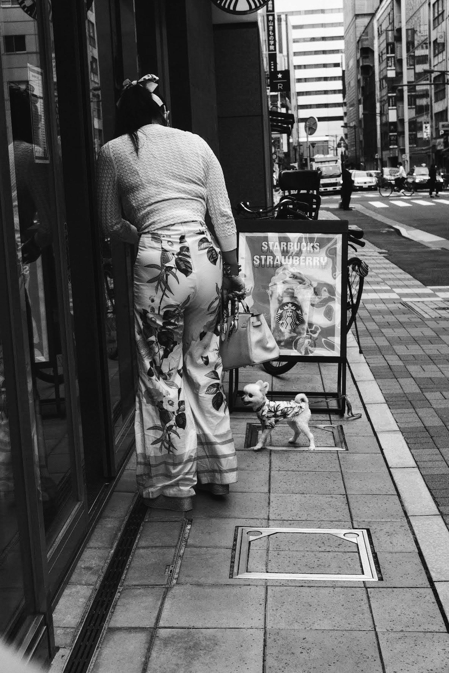 一位女士站在街道上的商店前面，黑白色的花裤子很显眼