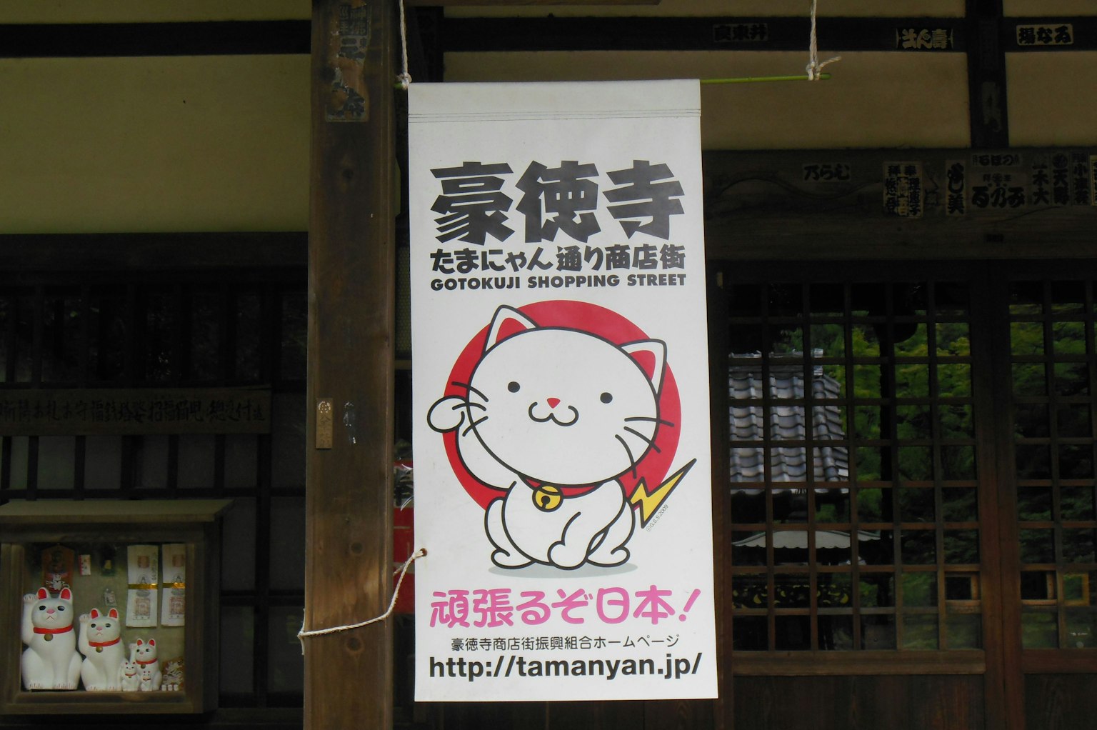 Papan yang menampilkan karakter kucing lucu dari Kuil Gotokuji dengan URL situs web