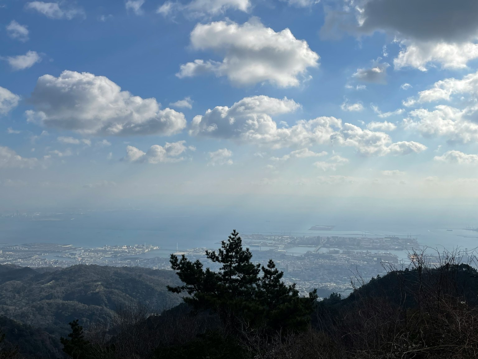 View from a mountain peak featuring a blue sky white clouds and a distant cityscape
