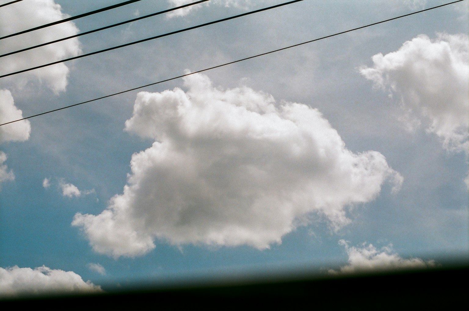 Nubes blancas esponjosas en un cielo azul con líneas eléctricas