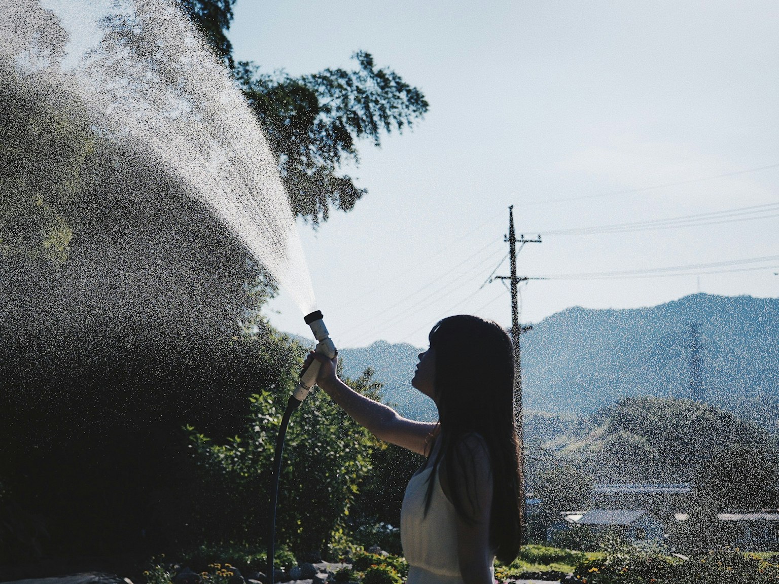 女性用水管浇水背景有山和电线