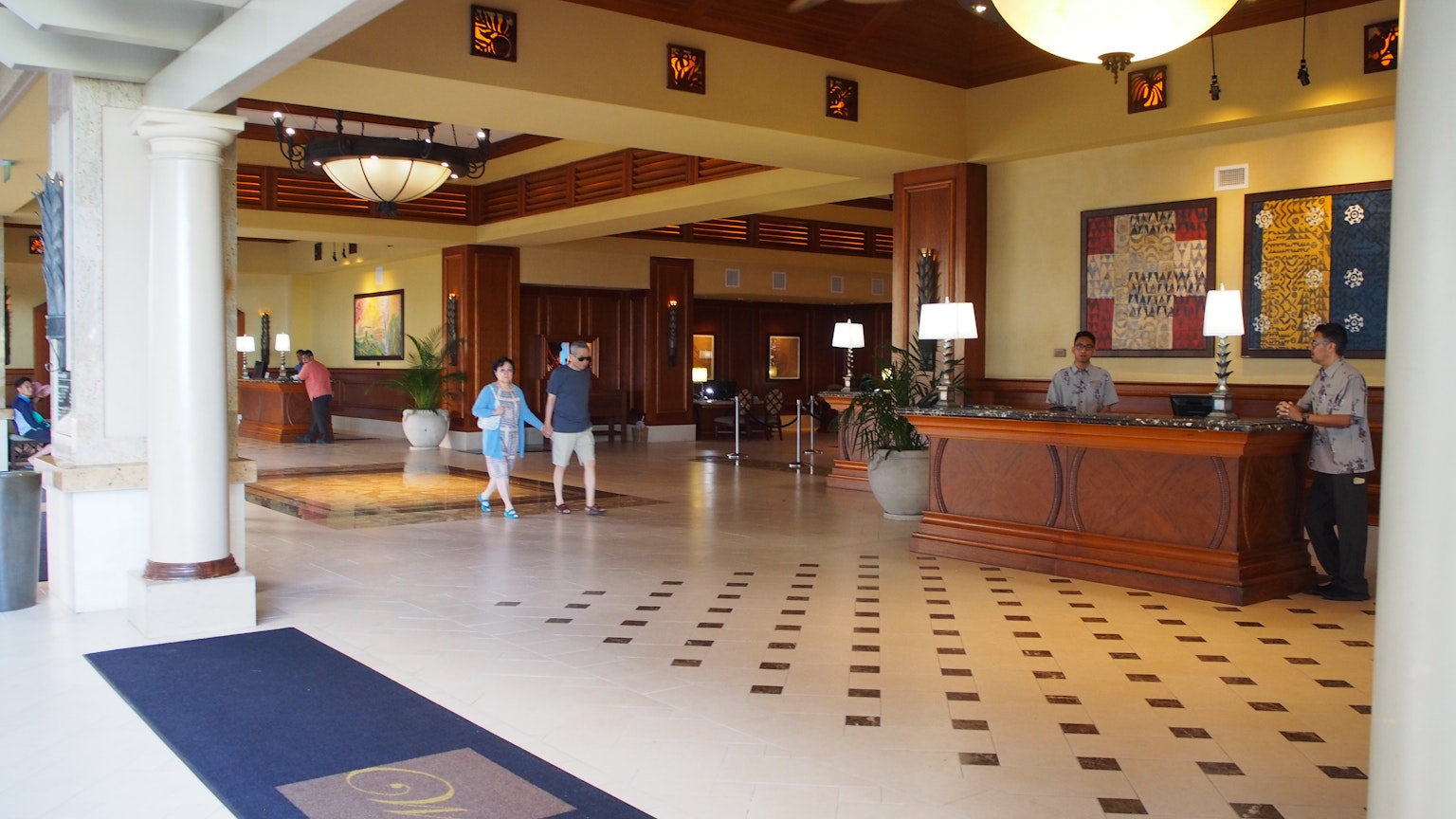 Die Hotellobby verfügt über einen Holzempfangstresen und einen gefliesten Boden mit mehreren wartenden Gästen