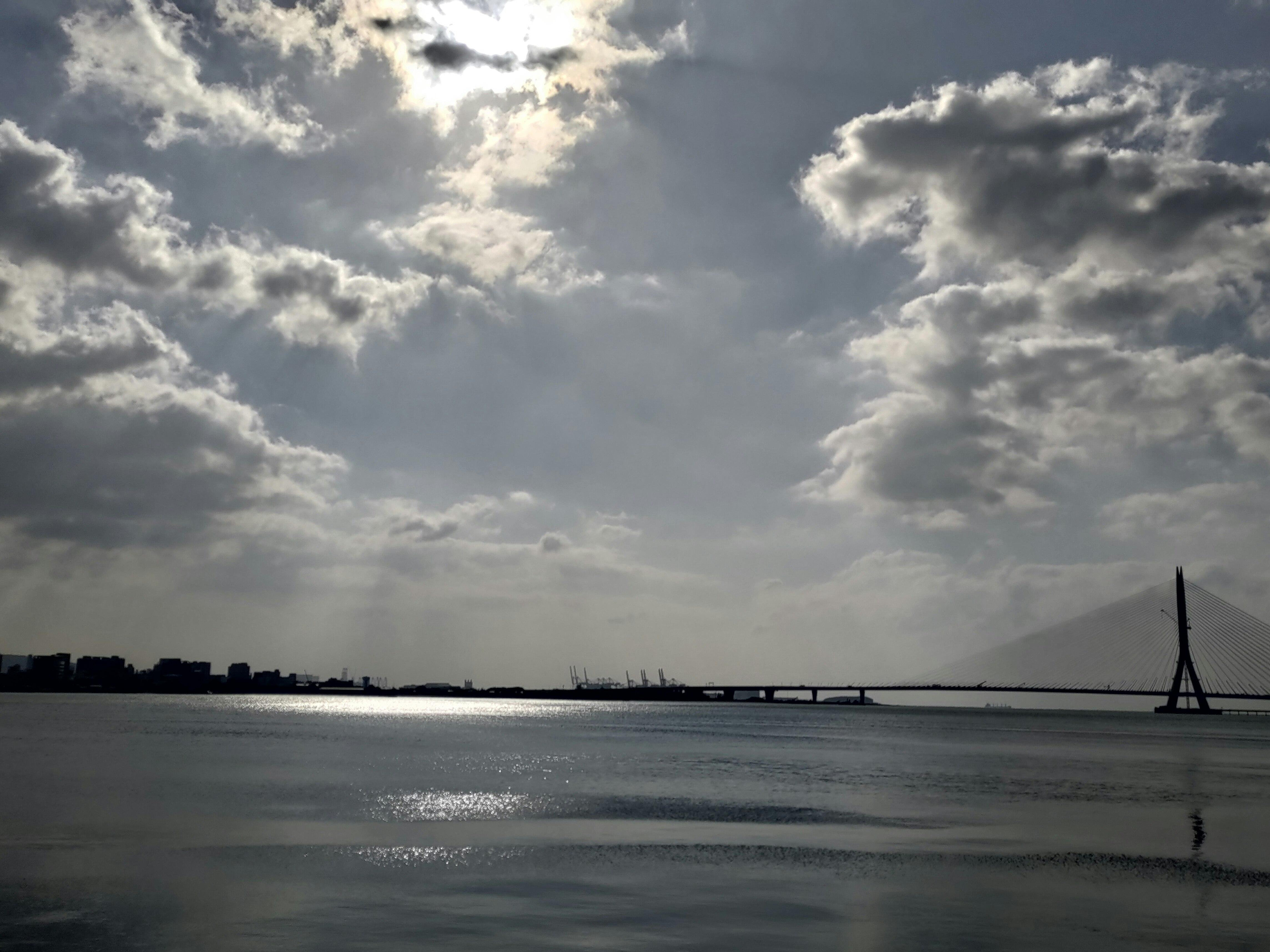 広い海面と雲の広がる空、遠くの橋のシルエット