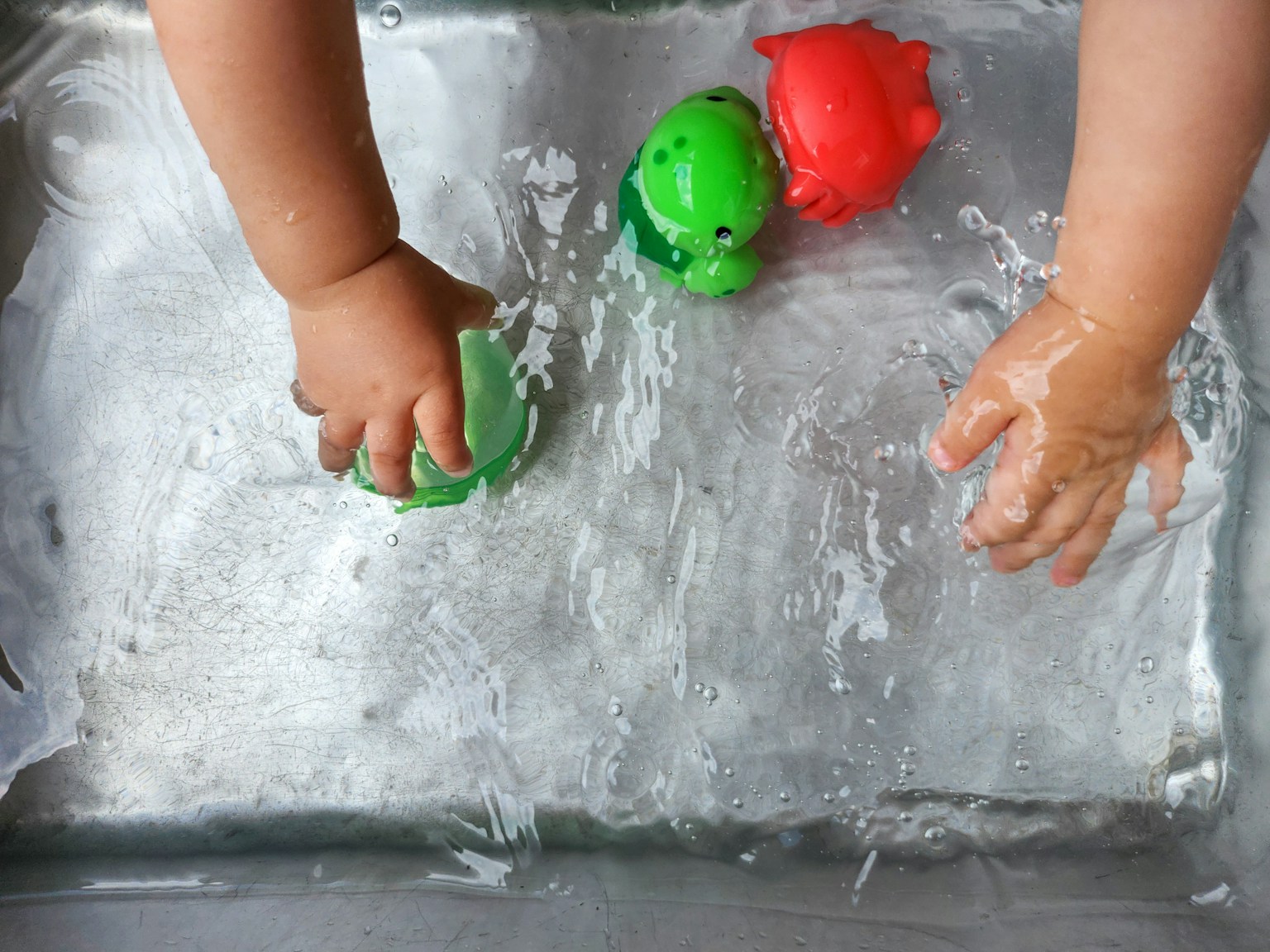 Mani di bambino che giocano con giocattoli a forma di rana verdi e rossi nell'acqua