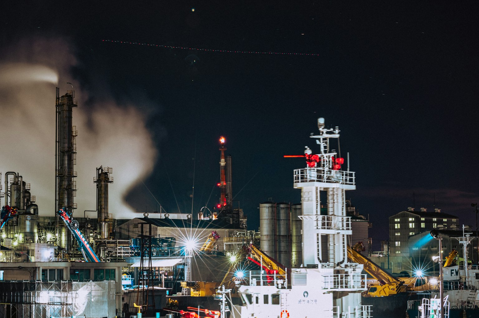 Nighttime industrial harbor scene featuring a ship and smoke