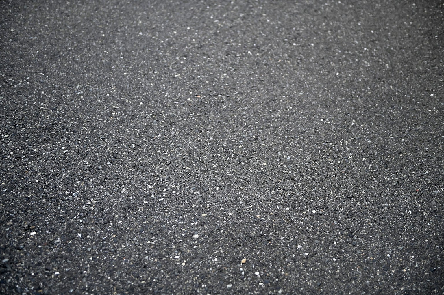 Surface noire d'asphalte avec de petites pierres et particules éparpillées