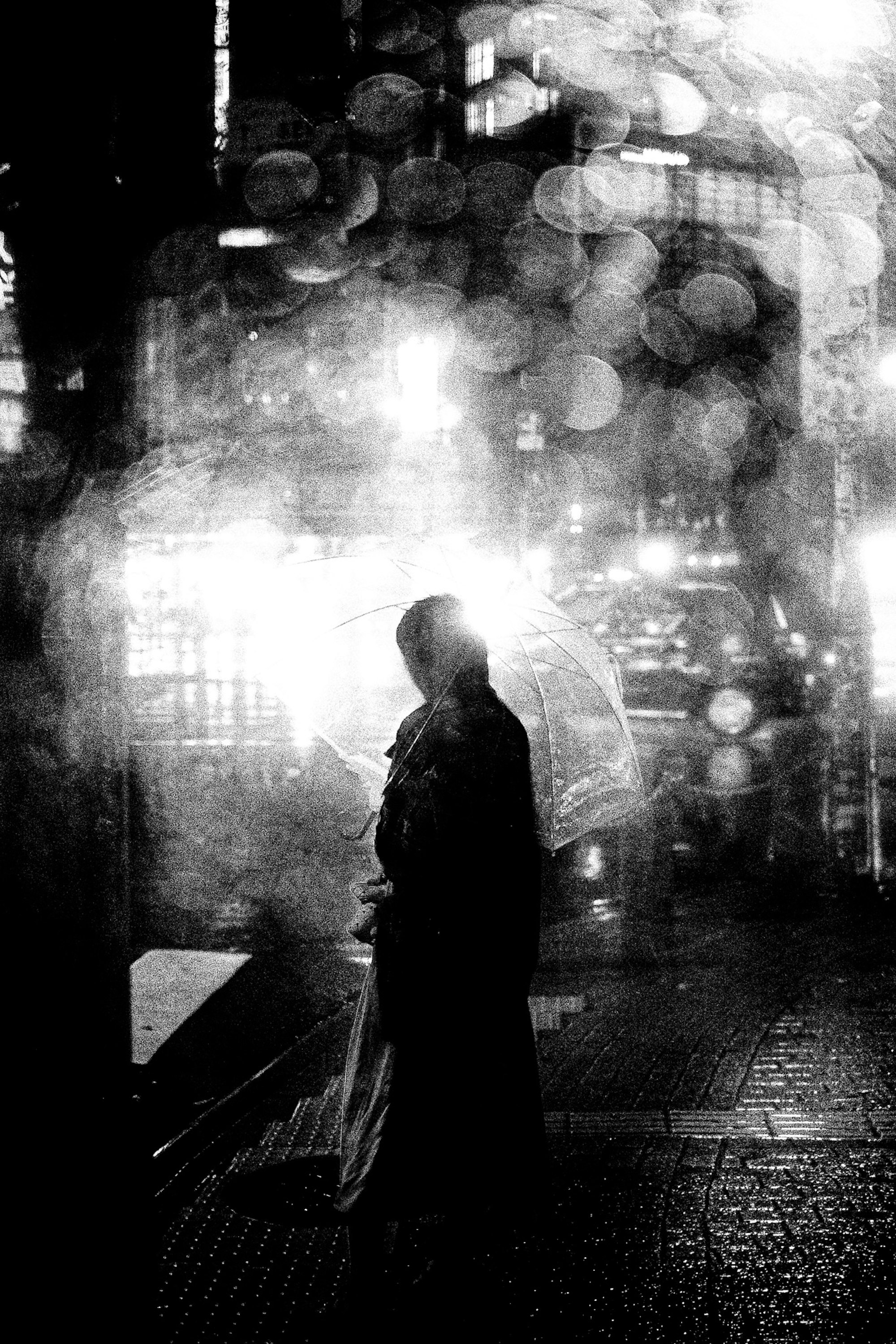 Silhouette en noir et blanc dans une ruelle avec des lumières de ville floues