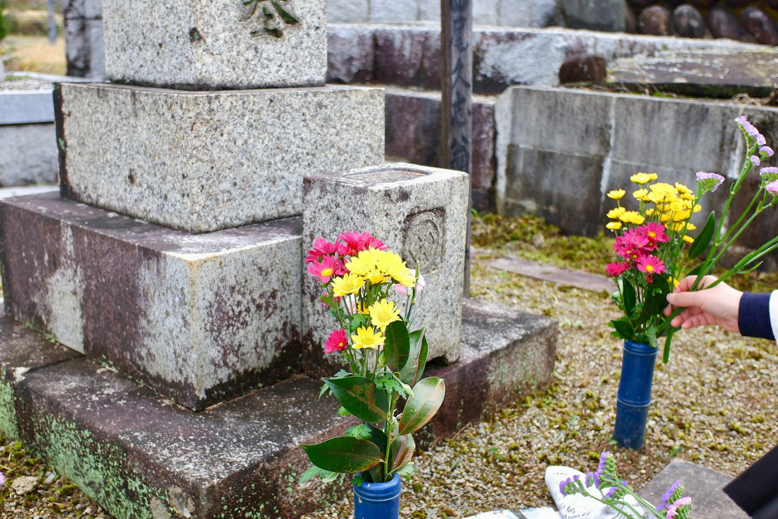 Eine Person, die sich nach Blumen an einem Grabstein streckt