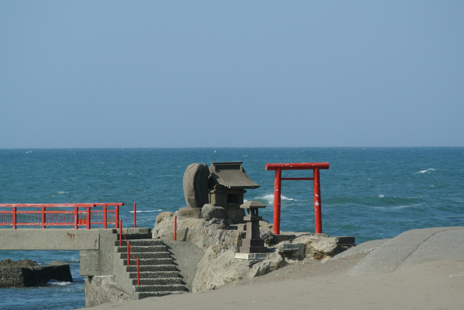 ทิวทัศน์ชายหาดที่มีมหาสมุทรและประตูโทริอิสีแดงล้อพลังน้ำและโครงสร้างหิน