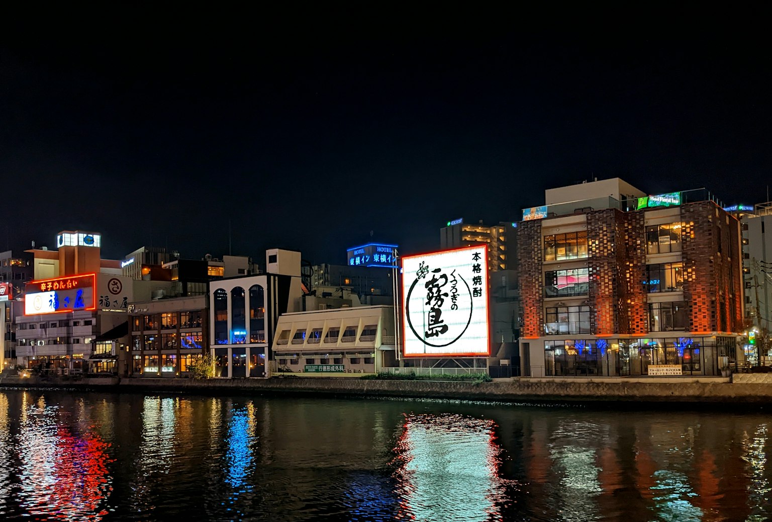 Scena urbana sul lungomare di notte con edifici illuminati e insegne al neon