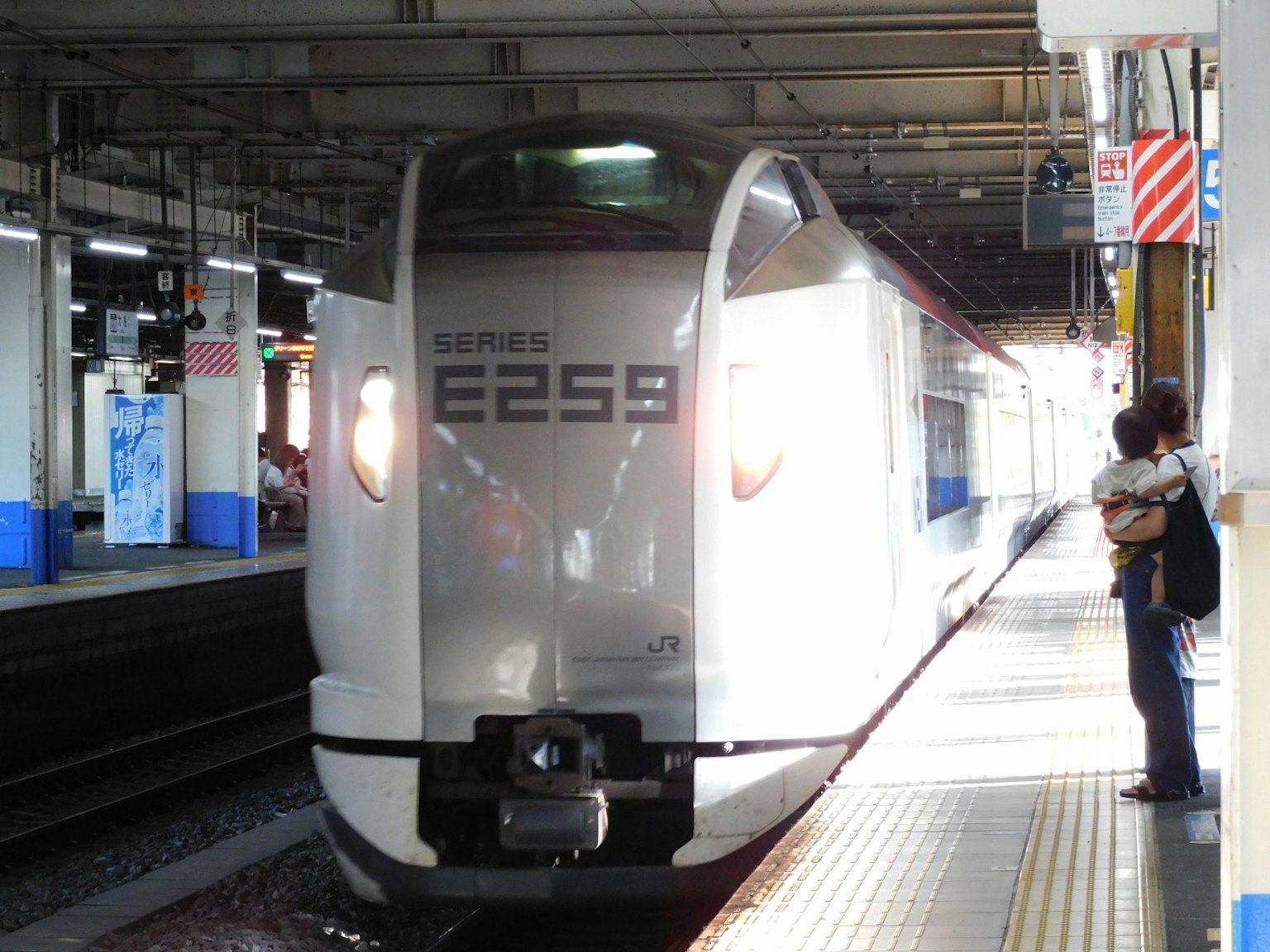 Un treno Shinkansen bianco che arriva in una stazione con un passeggero in attesa