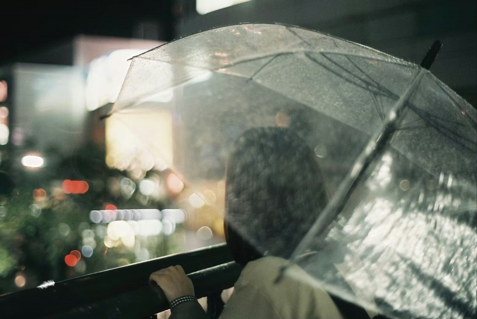Une personne tenant un parapluie transparent regardant la ville la nuit