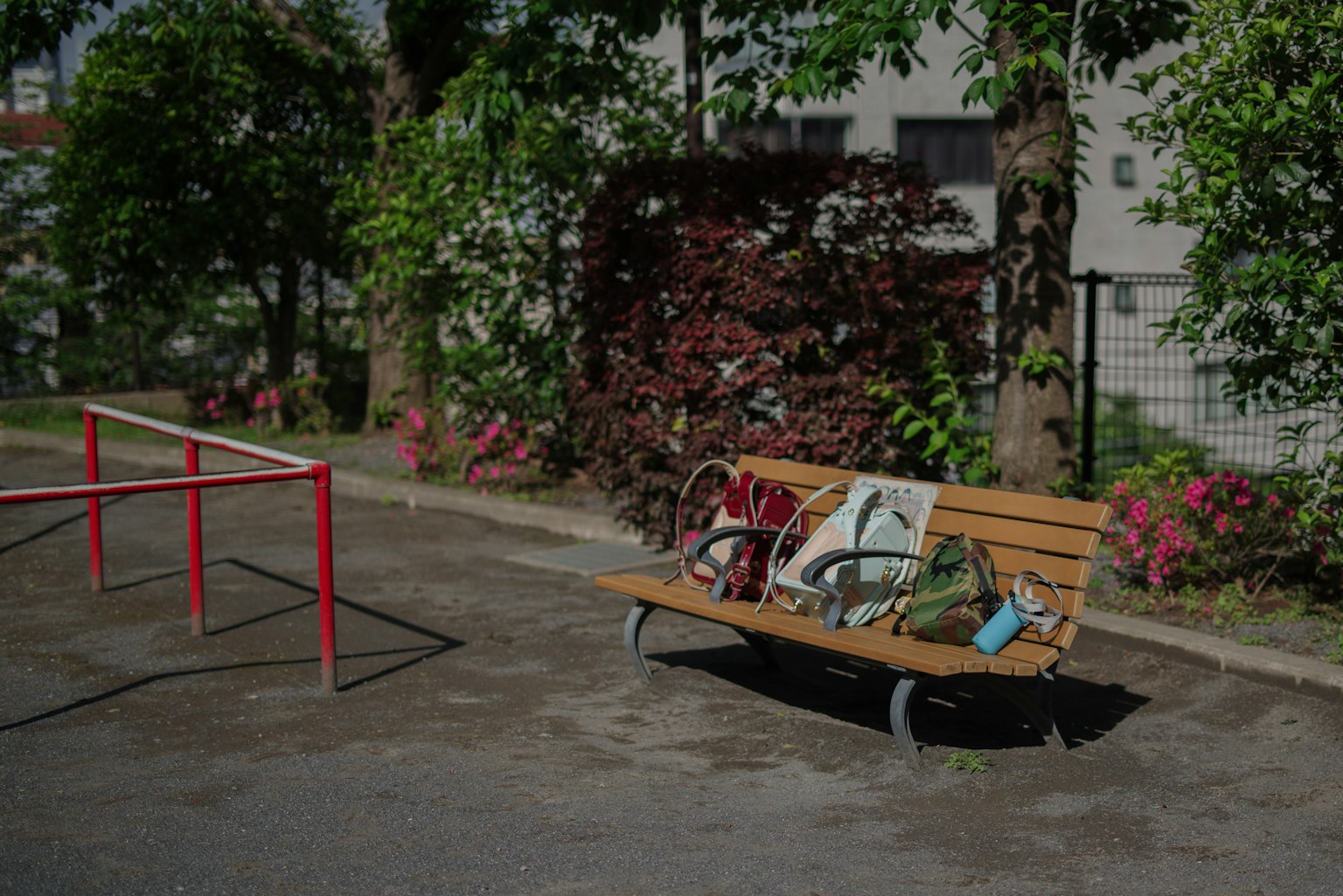 A park bench with a bicycle and bag resting on it surrounded by green trees and flowers