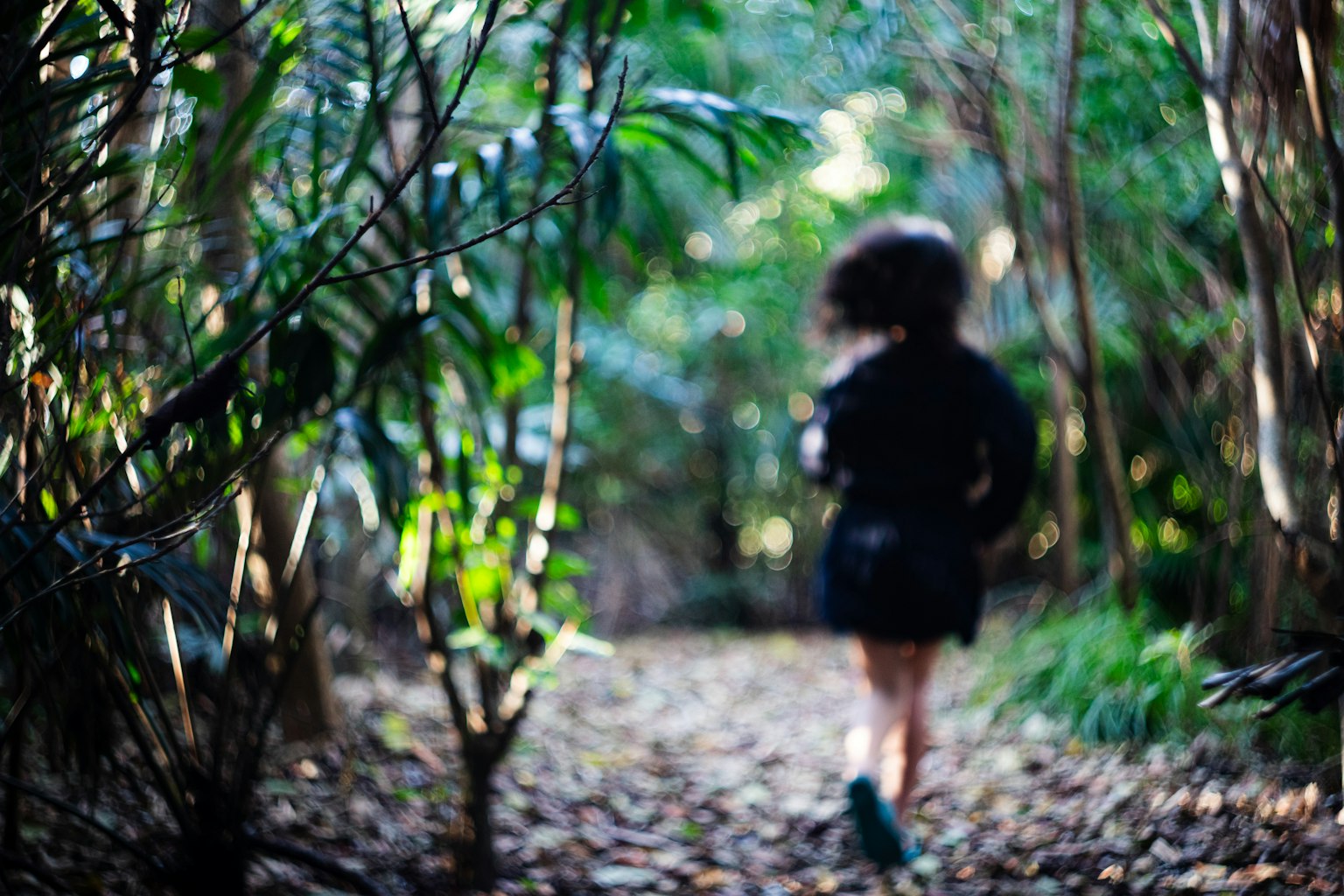 Eine Frau läuft auf einem Waldweg umgeben von Grün und fallenden Blättern