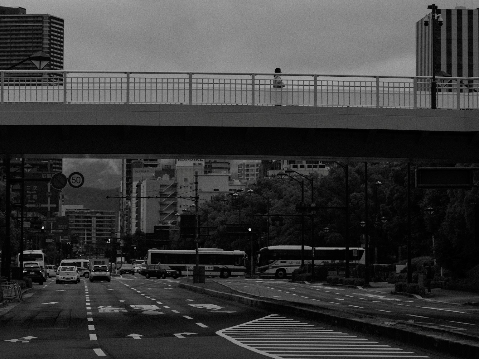 ทิวทัศน์ถนนในเมืองพร้อมสะพานในโทนสีขาวดำที่มีคนยืนอยู่บนสะพาน