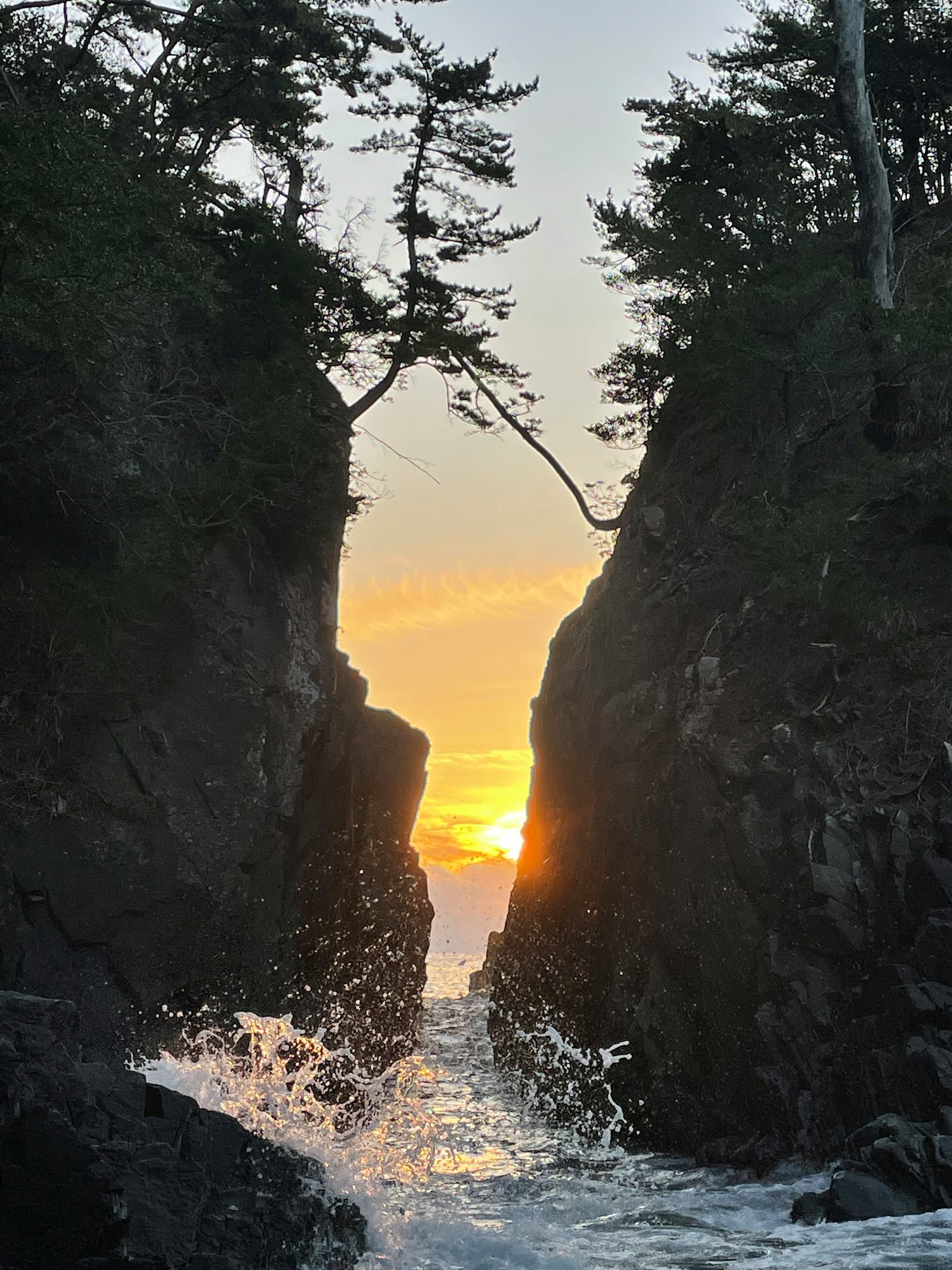 Scenic view of the sun setting between rocky cliffs and ocean waves