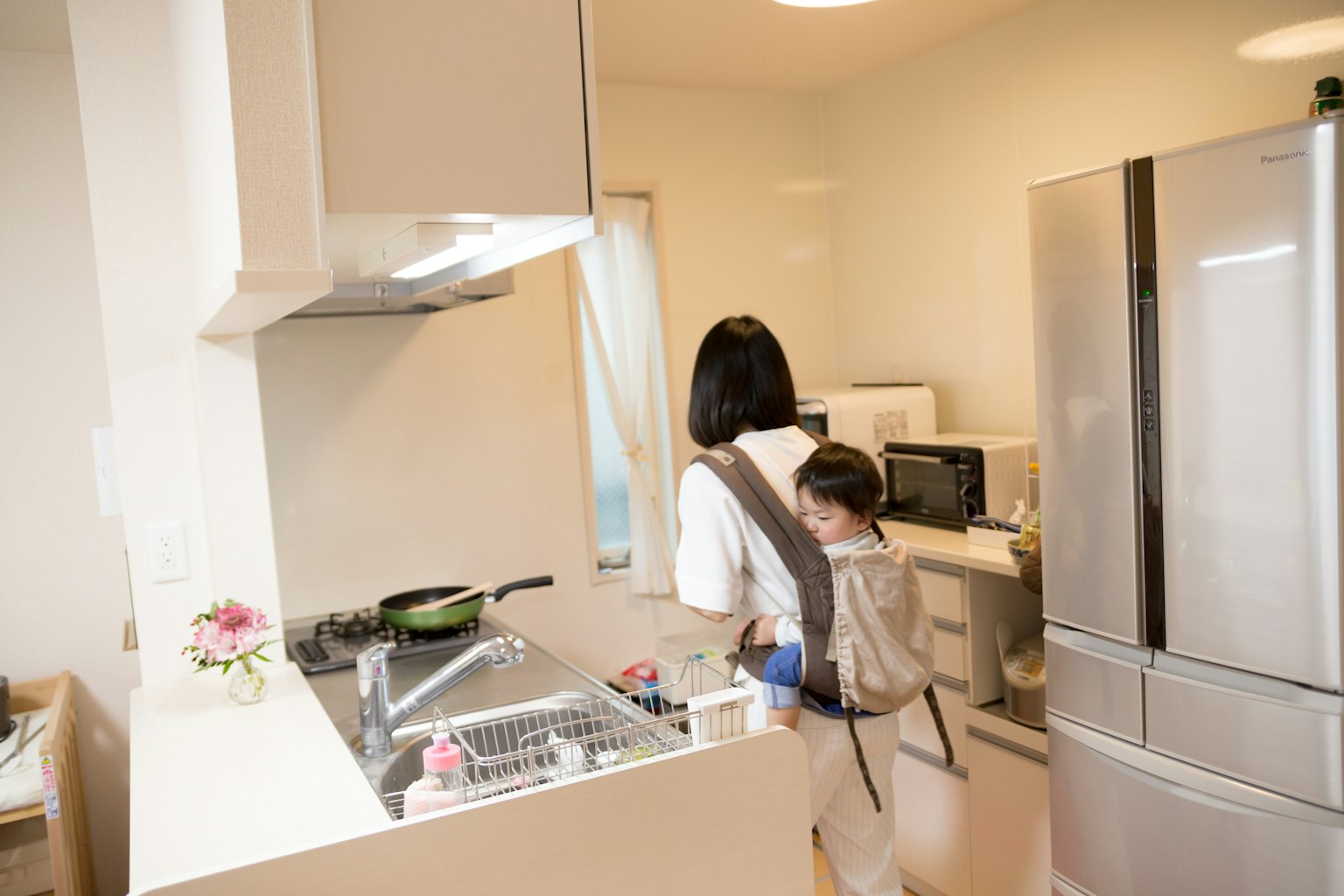 Une mère cuisinant dans une cuisine lumineuse avec un enfant sur le dos