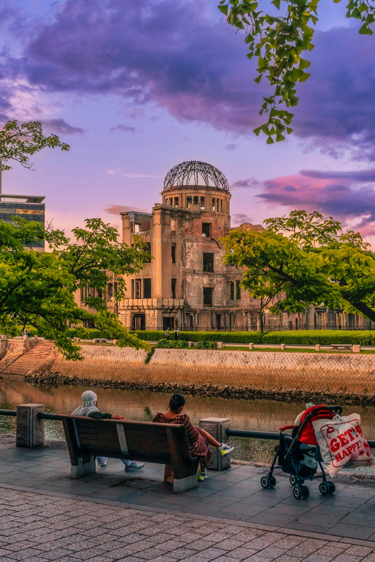 People sitting on a bench with the Hiroshima Peace Memorial and river in the background