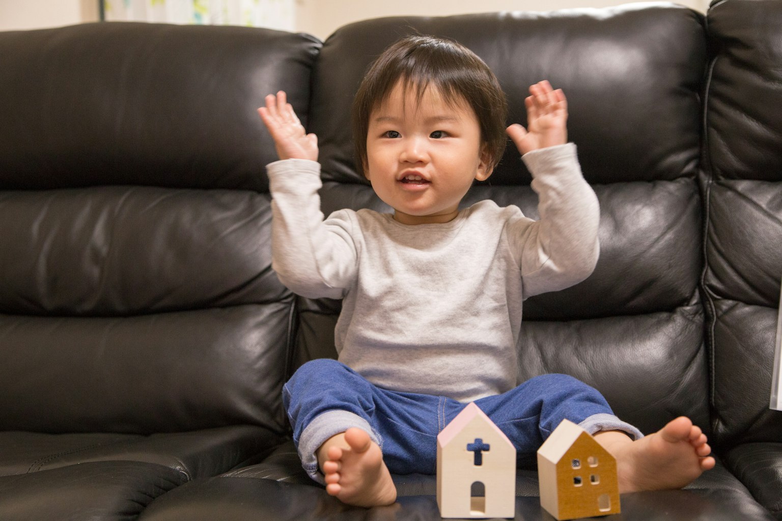 Toddler sitting on a sofa raising hands with a smile
