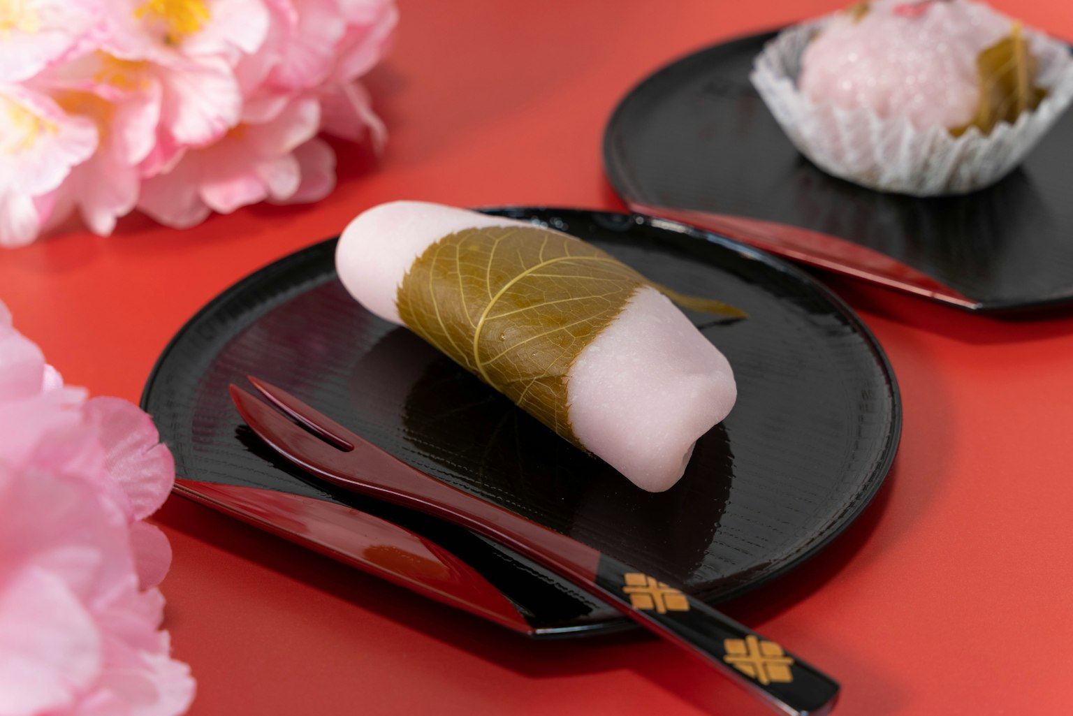 Kue Jepang di piring hitam dengan latar belakang bunga sakura