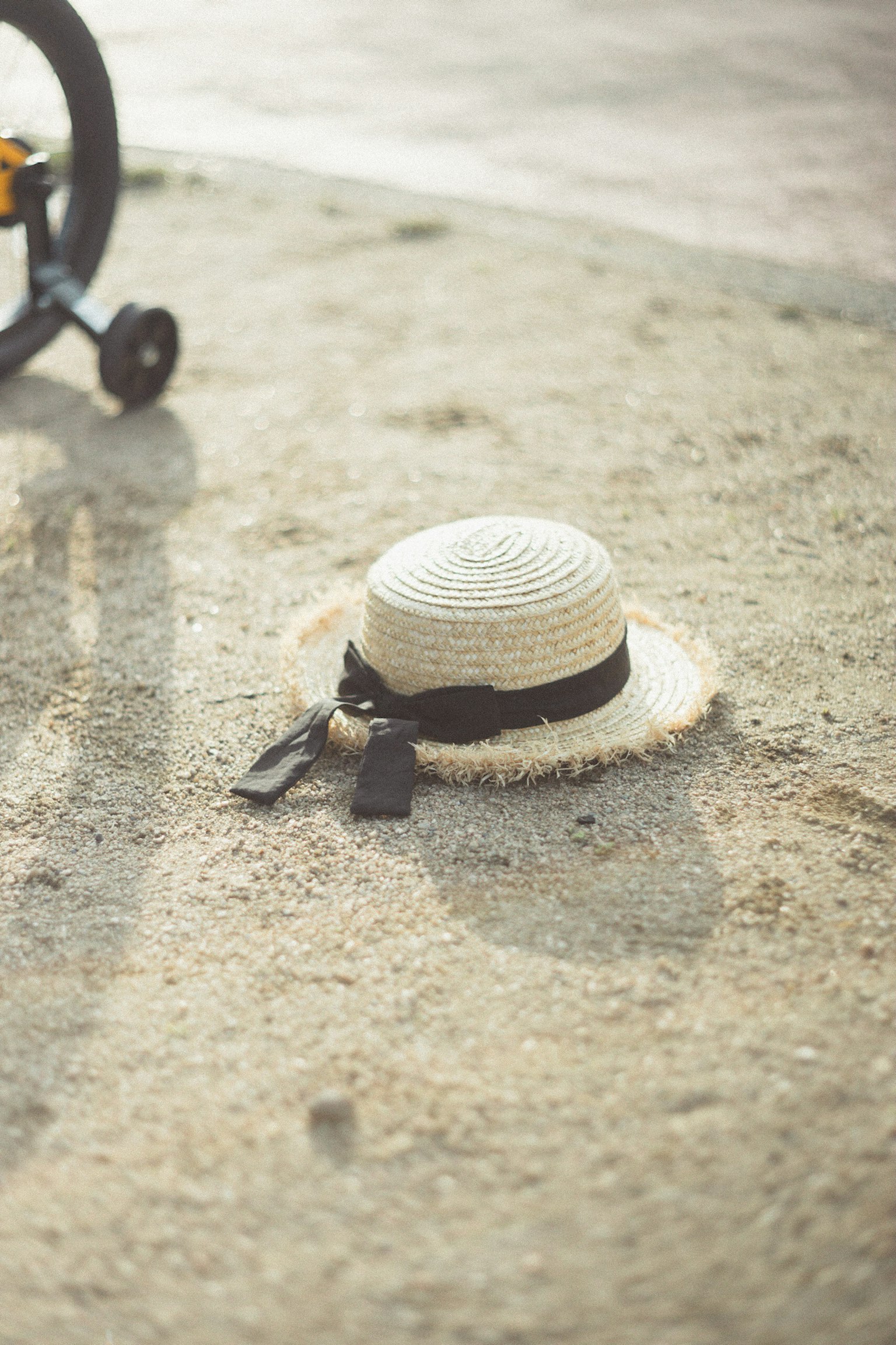 Chapeau de paille avec un ruban noir posé sur le sol sablonneux