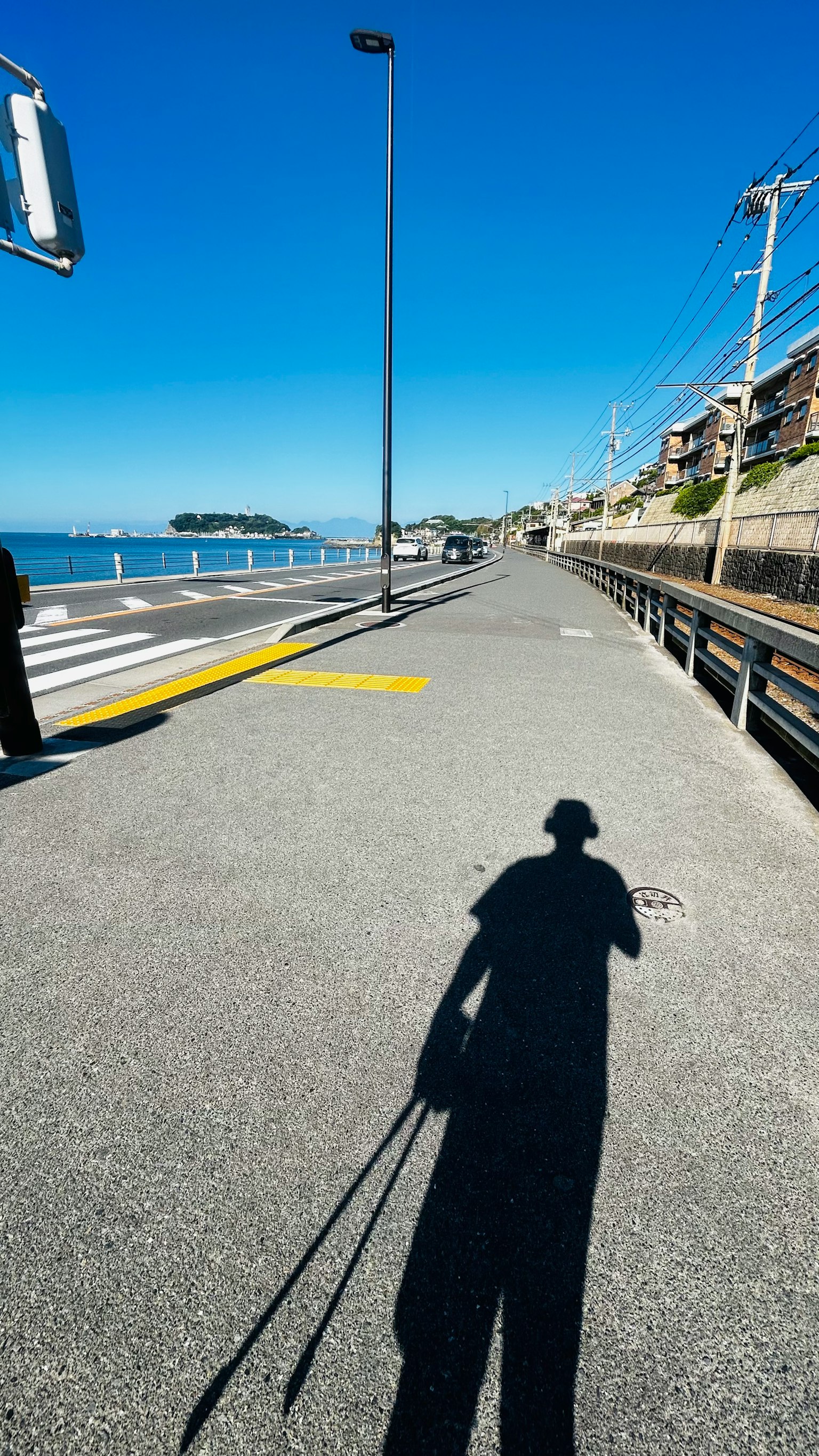 Ombra di una persona su una passeggiata costiera sotto un cielo blu chiaro