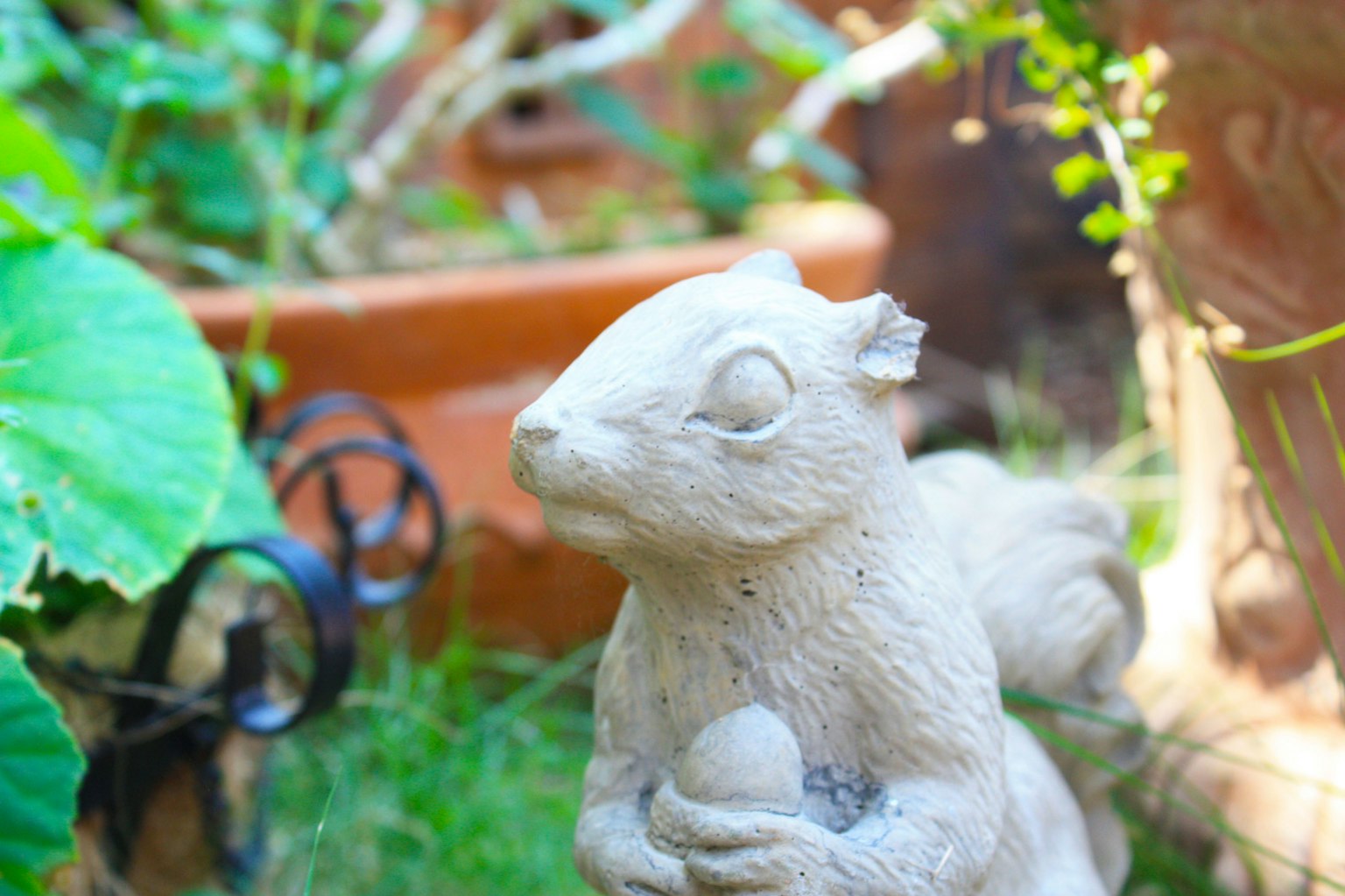 Una statua di scoiattolo in pietra in un giardino circondata da piante verdi