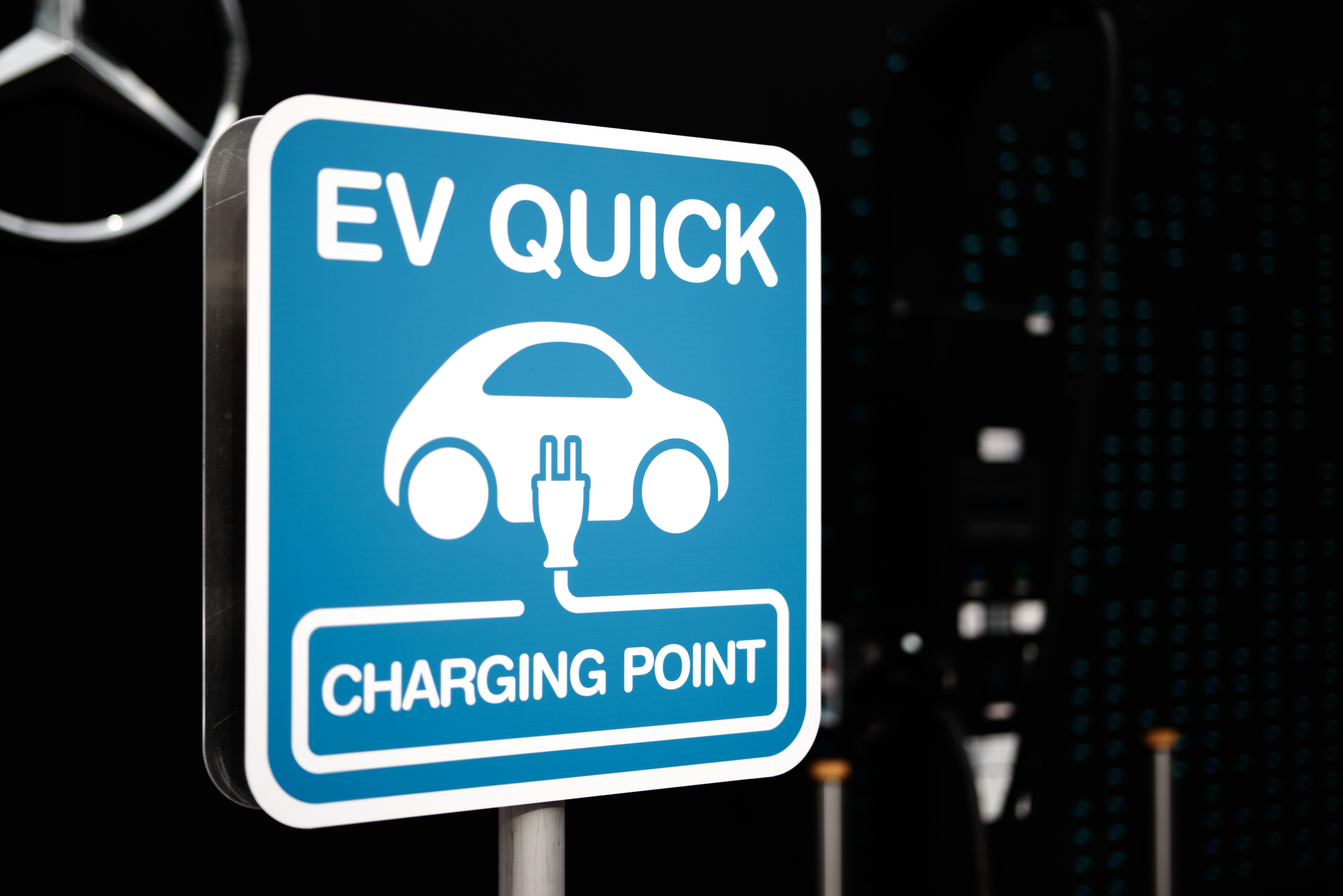 Schild „EV QUICK“ Ladestation mit nächtlicher Skyline