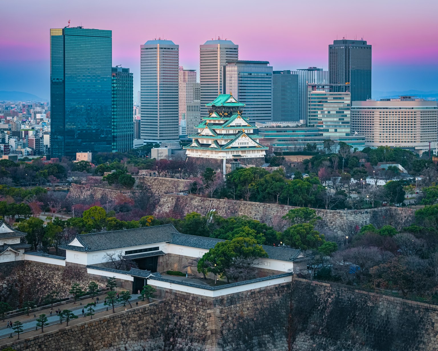 Pemandangan panorama Kastil Osaka dengan gedung pencakar langit modern saat matahari terbenam