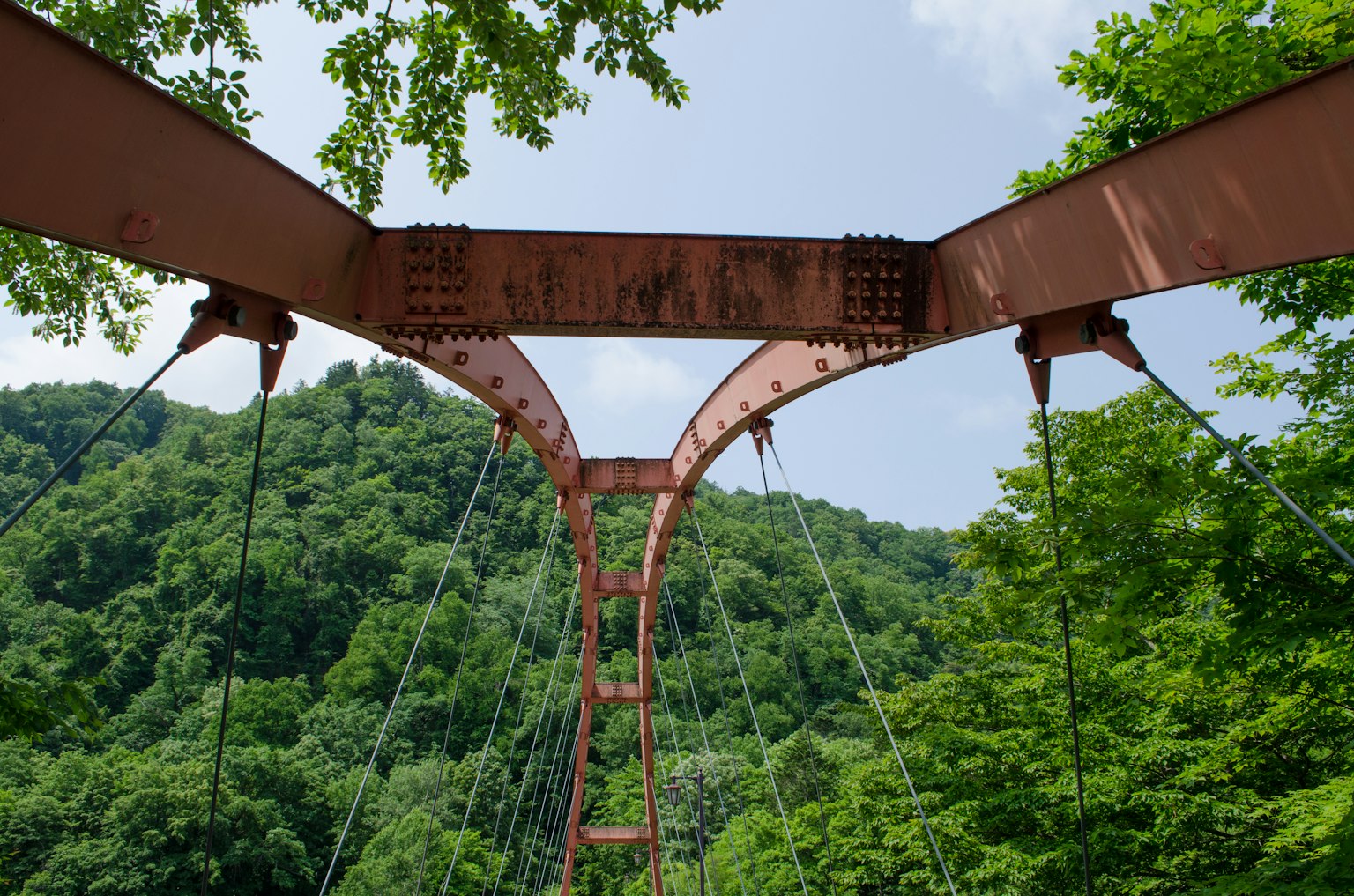 Image d'une structure de pont suspendu vue d'en bas entourée de montagnes vertes