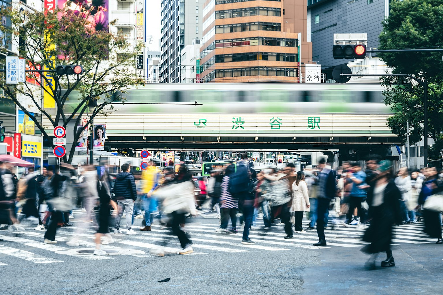Belebte Kreuzung in Tokio mit verschwommenen Fußgängern und einem vorbeifahrenden Zug