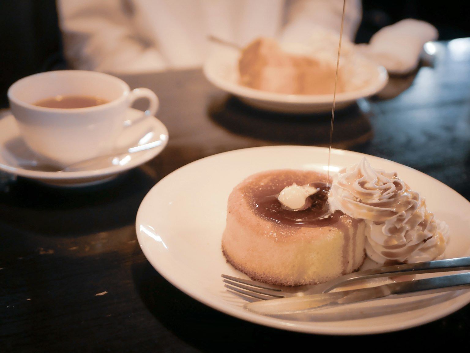 Une assiette avec un gâteau garni de crème et de sirop et une tasse de café