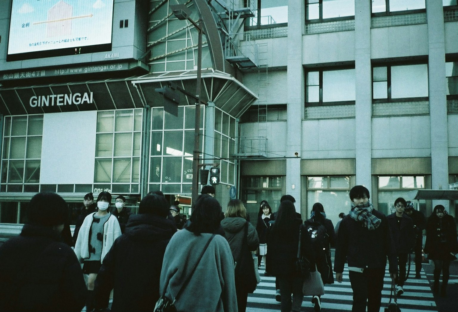 Personas cruzando la calle frente a un edificio moderno con el letrero GINTENGAI