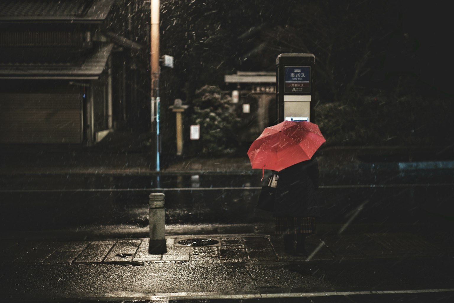 一個人手持紅色雨傘在夜晚的雨中站在電話亭前